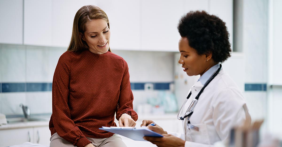 Happy woman going through her medical data with black female doctor at clinic.